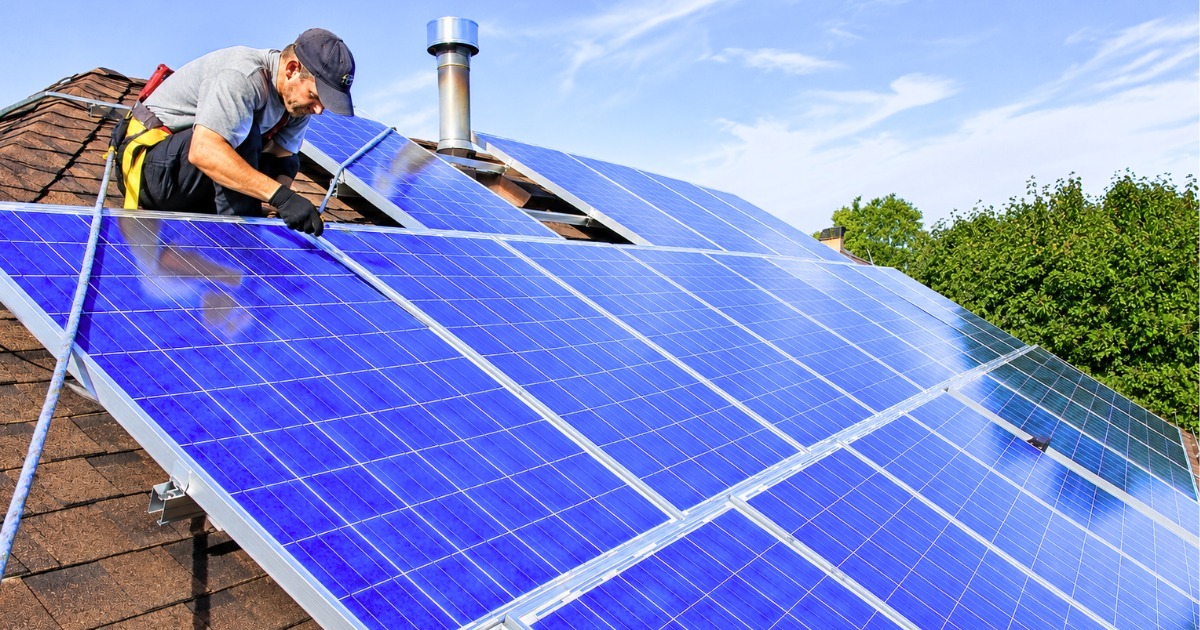 Solar panel installation by an expert technician mounting blue solar panels on a residential shingle rooftop