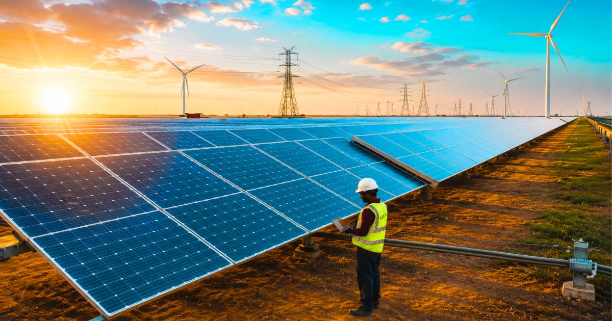 Waaree solar panel farm with technician and wind turbines at sunset